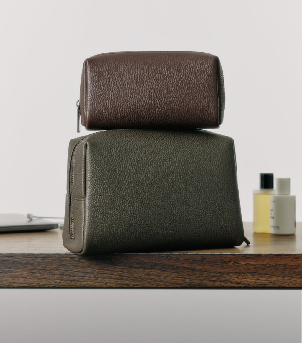 Two toiletry bags stacked on a wooden surface with small bottles in the background.