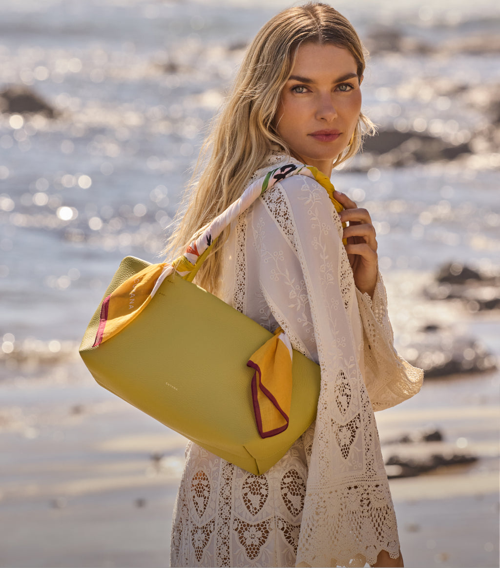 Person on beach with a bag over shoulder, wearing a patterned dress.