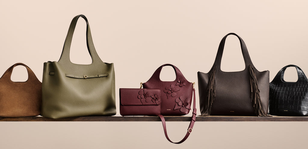Five handbags displayed on a shelf, including a croc-embossed leather one on the right.