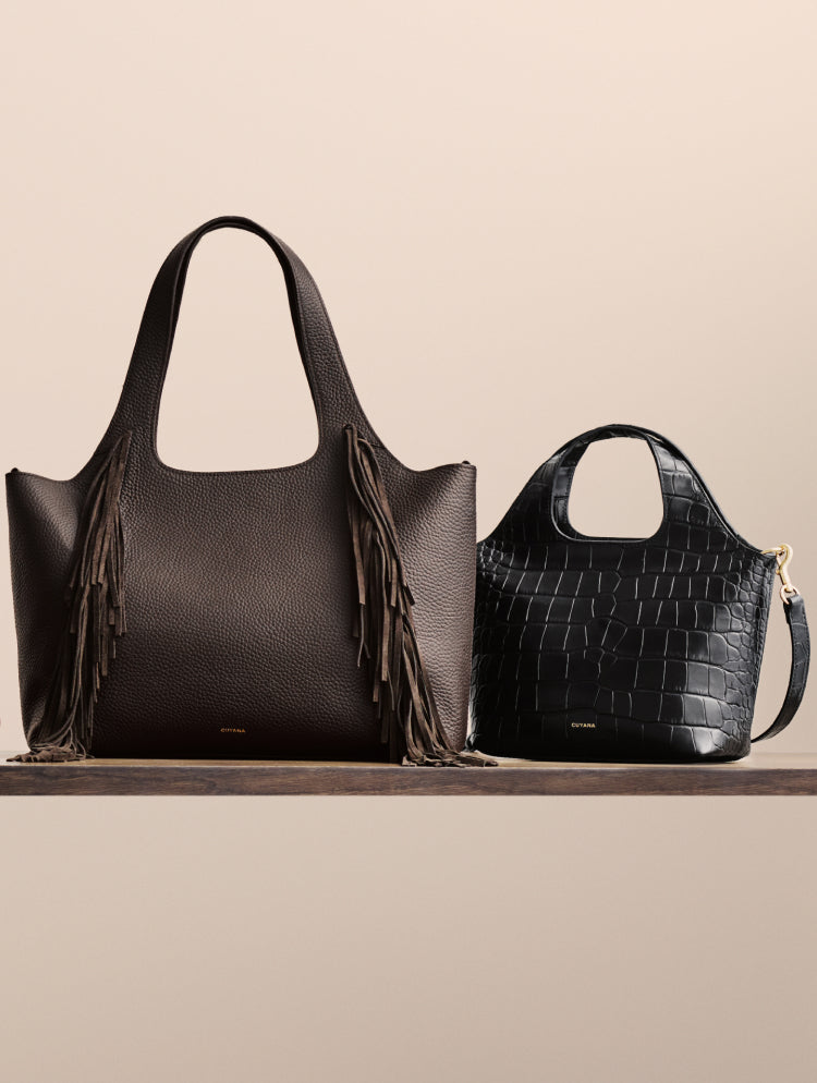 Two handbags on a surface, one with fringe, the other with croc-embossed leather.