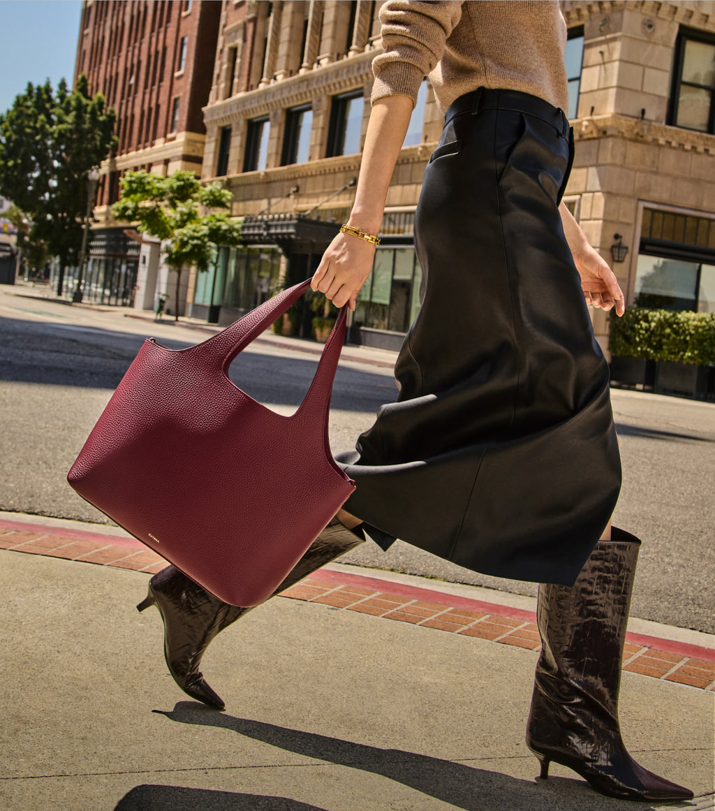 Person walking with a handbag and wearing boots and a skirt in an urban setting.