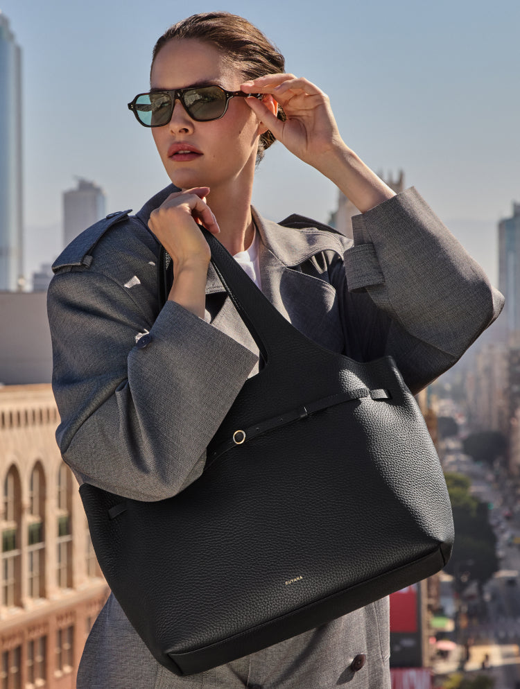 Woman in coat holding a large handbag on a city rooftop.