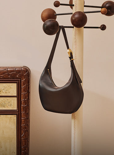 Shoulder bag hanging on a stand near furniture with croc-embossed leather decor.