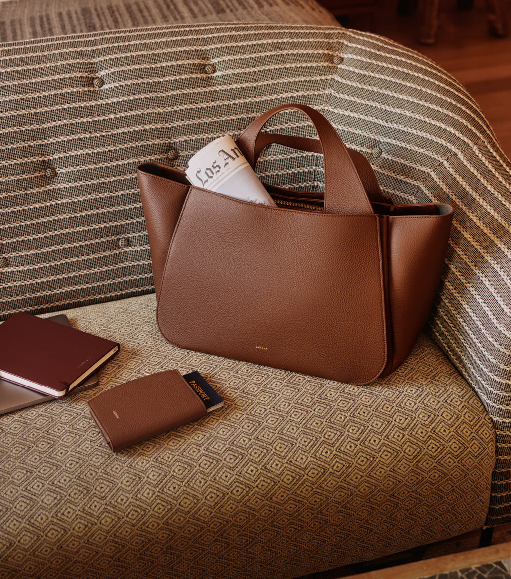 Travel bag on couch with a notebook, wallet, and newspaper.