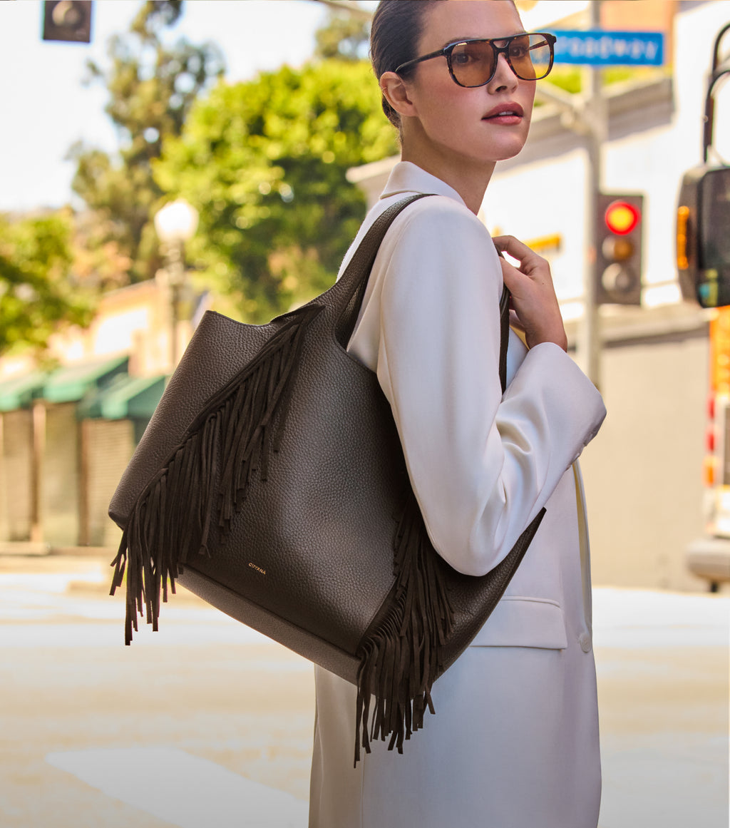 Person in sunglasses holding a fringed handbag outdoors.