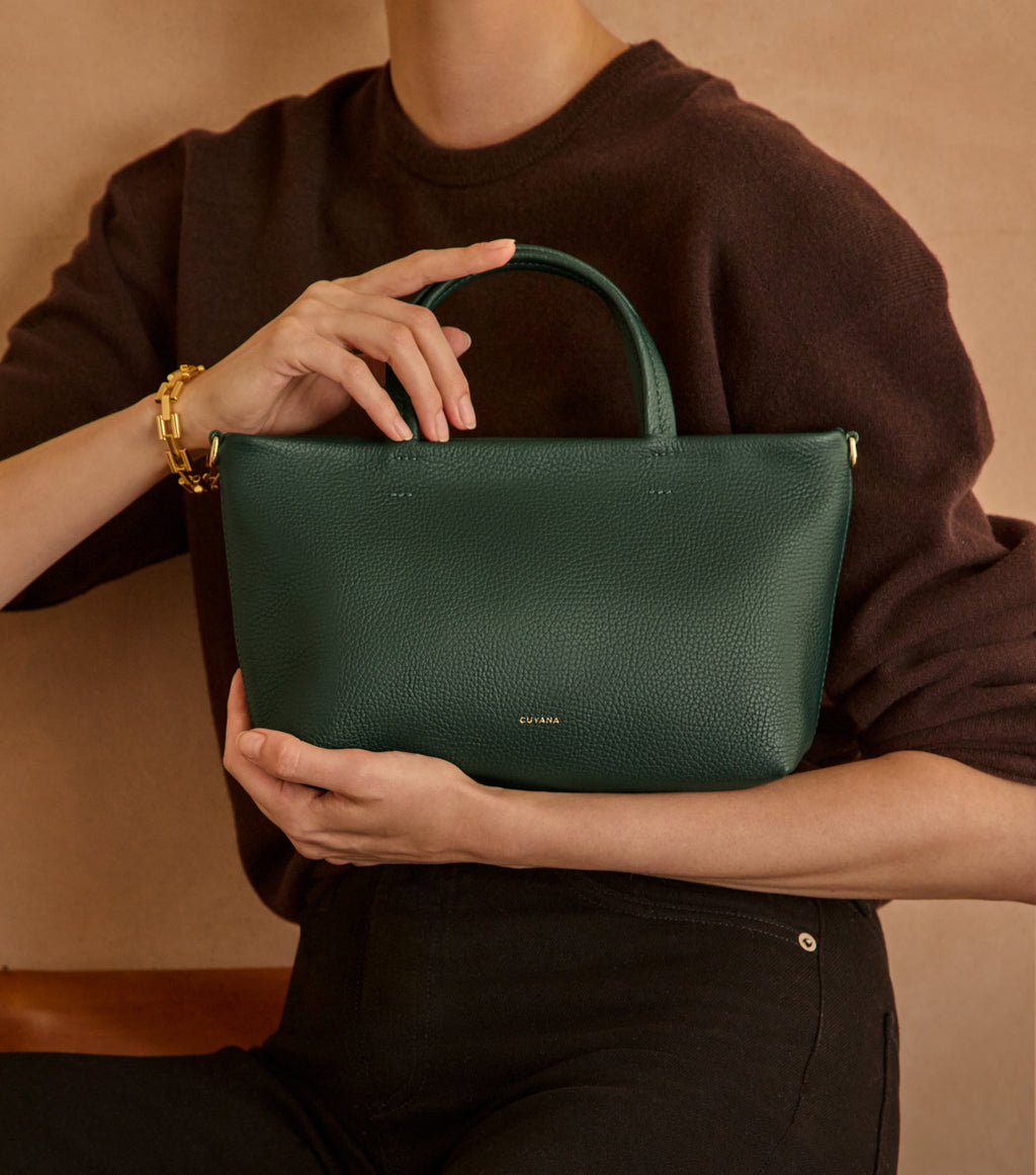Person holding a handbag with one hand on the handle, wearing a bracelet.