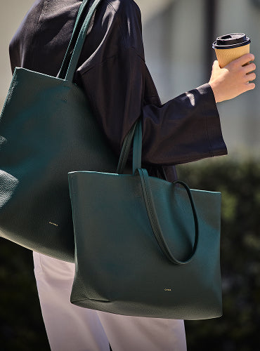Person holding coffee cup and two large tote bags.