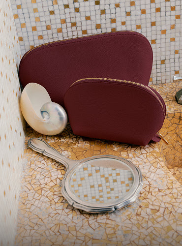 Two pouches with seashell and handheld mirror on mosaic surface.