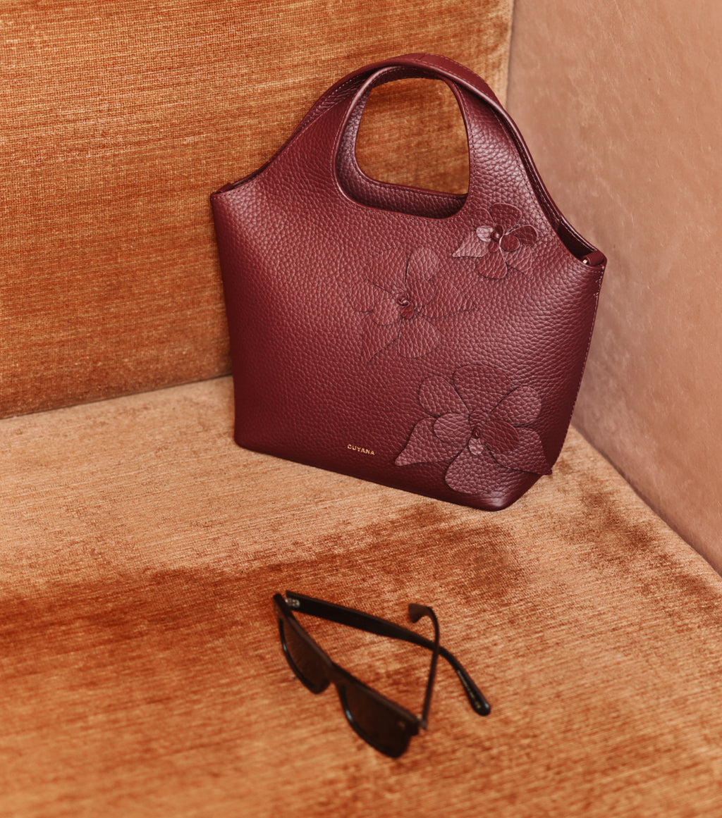 Handbag with floral design on a couch next to sunglasses.