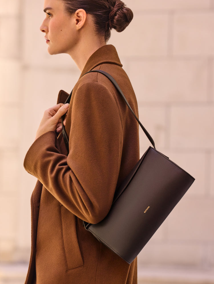 Person holding a shoulder bag while wearing a coat.