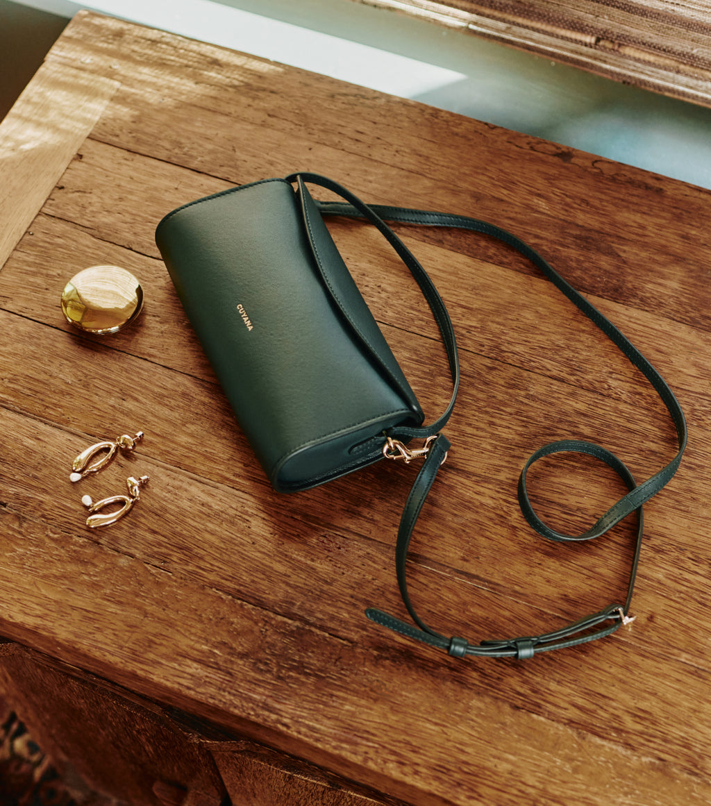 Handbag, earrings, and small round container on a wooden table.