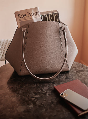 Tote bag with magazines on a table beside a smartphone and a closed notebook.