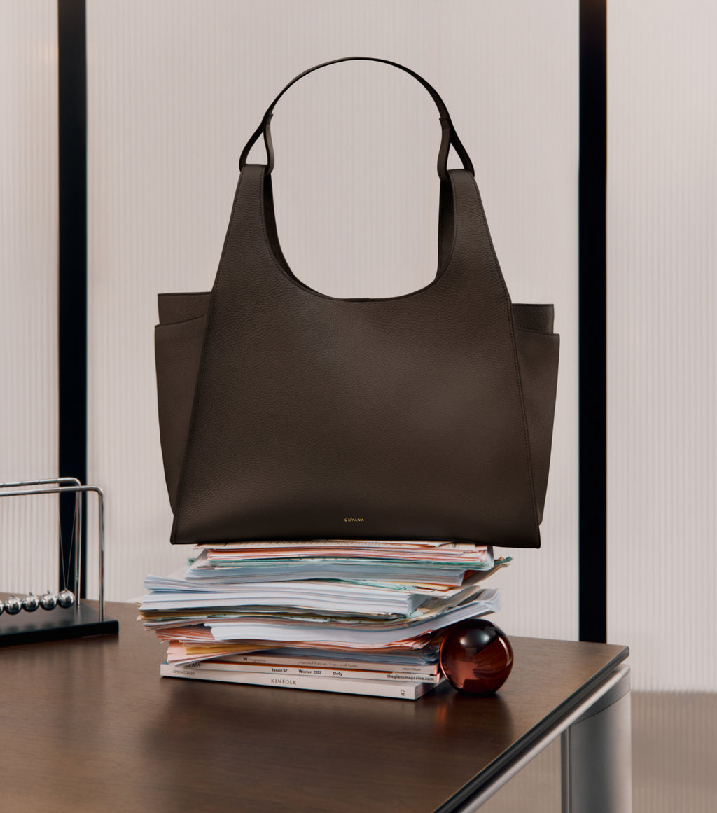 Large handbag on top of a stack of papers on a desk.