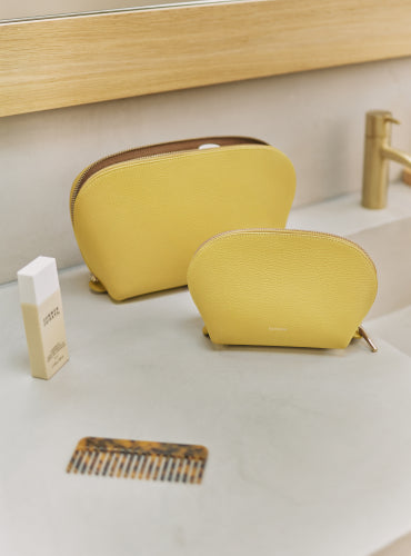 Two toiletry bags on a bathroom counter with a comb and a small bottle.