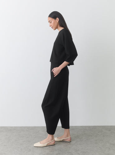 Woman standing in side profile wearing a two-piece outfit and flats.