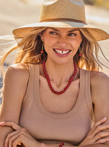 Woman wearing a hat, tank top, and necklace, smiling outdoors.