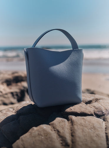 Handbag on rocks by the beach with ocean in background.