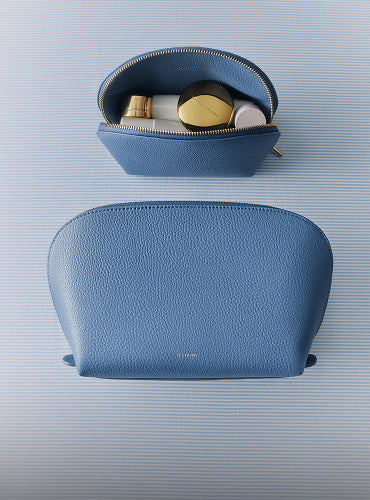 Two makeup bags, one open with items inside, on a striped surface.