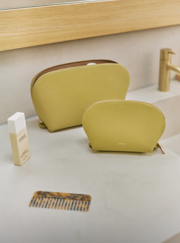 Two cosmetic pouches on a counter with a comb and skincare product nearby.