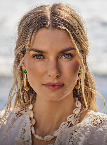 Person wearing shell necklace and earrings by the sea.