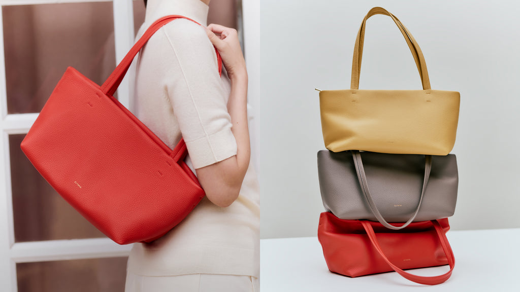 Person holding a tote bag, next to stacked tote bags on a surface.