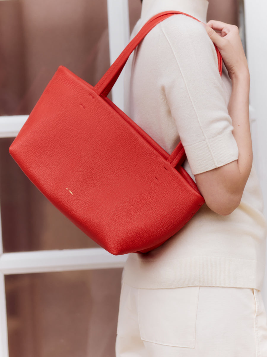 Person holding a large tote bag on their shoulder indoors.