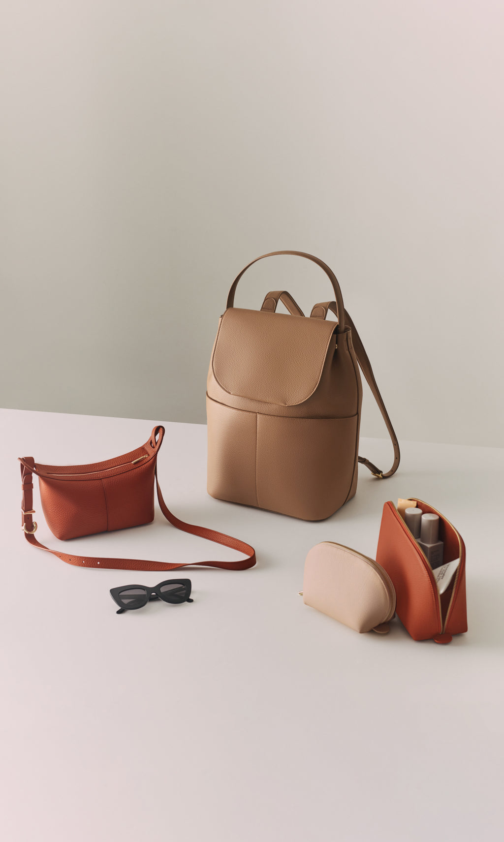 Backpack, belt bag, sunglasses, small pouch, and open pouch with items on a table.