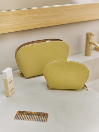 Two cosmetic bags on a bathroom counter with a comb and lotion bottle nearby.