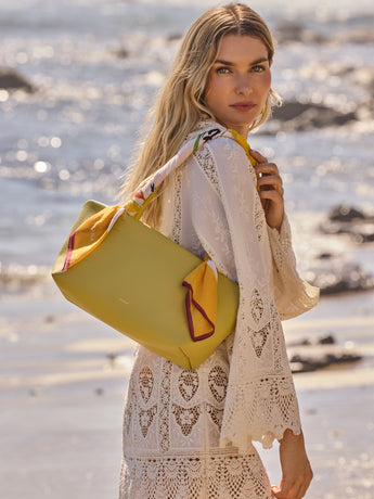 Woman on beach with yellow bag wearing a lace dress.