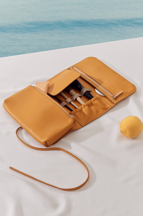 Makeup brushes in an open pouch on a table next to a lemon.