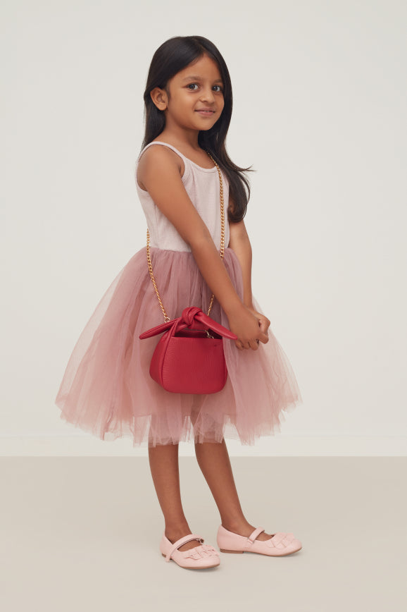 Young girl standing with a handbag and wearing a tutu dress and shoes.