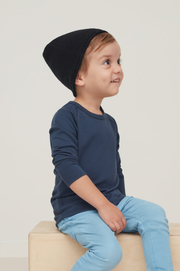 Young child wearing a beanie sits on a cube, looking to the side.