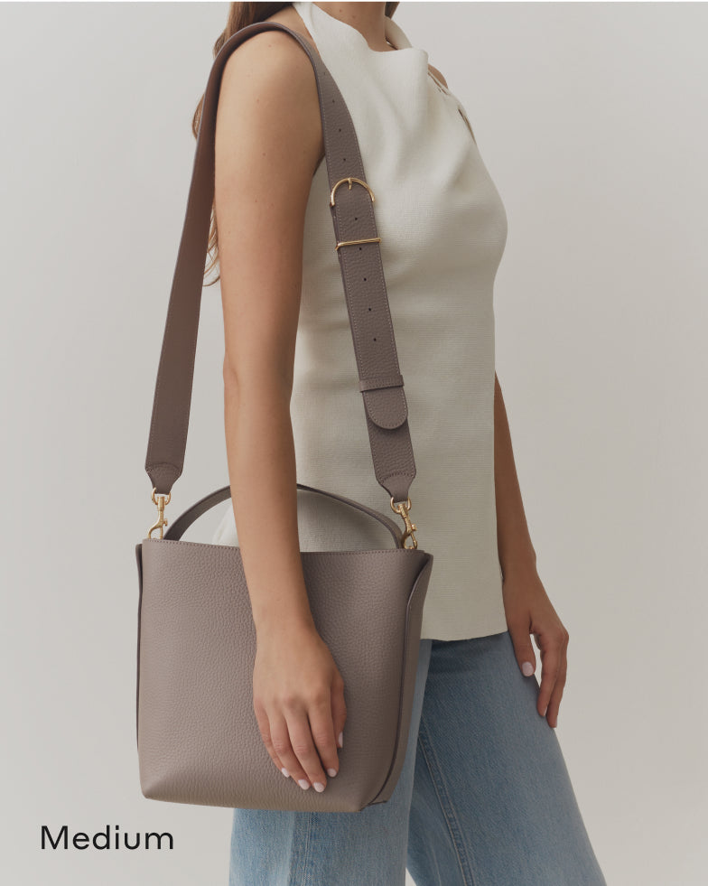 Person carrying a medium-sized shoulder bag with a wide strap.