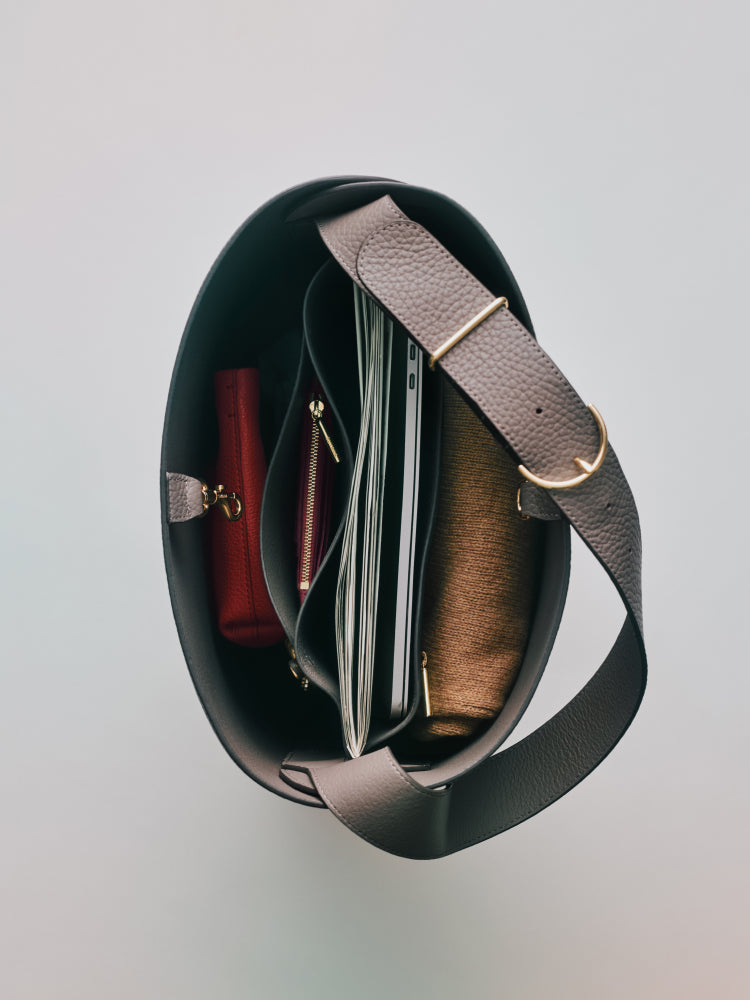 Top view of an open handbag showing various items including a laptop and a zippered pouch inside.