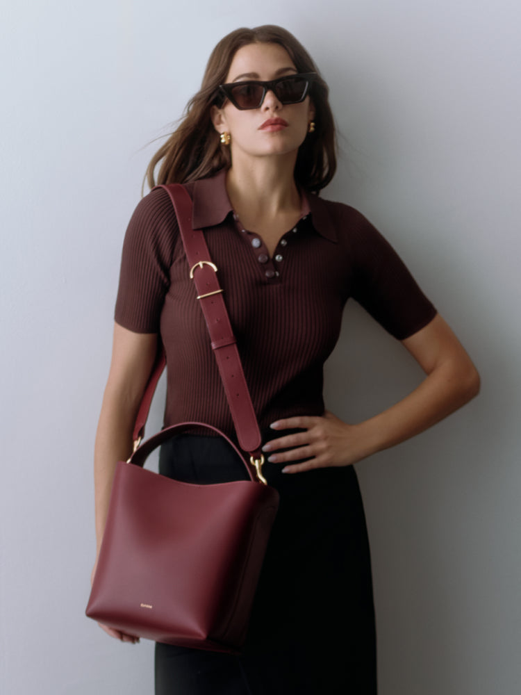 Woman wearing sunglasses, collared shirt, skirt, and carrying a shoulder bag.