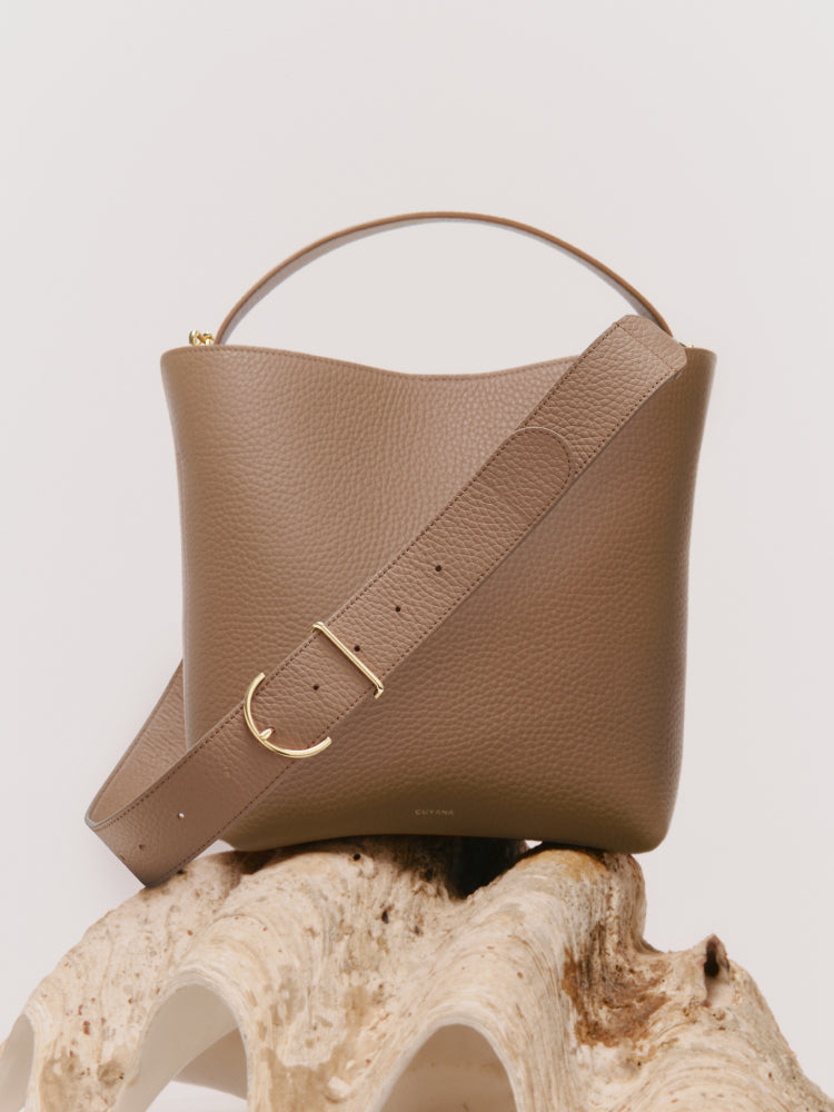 A handbag with a wide strap and a handle displayed on a textured surface.