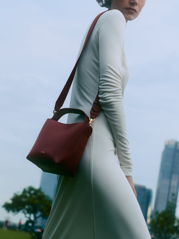 Person in a long dress with a handbag standing outside.