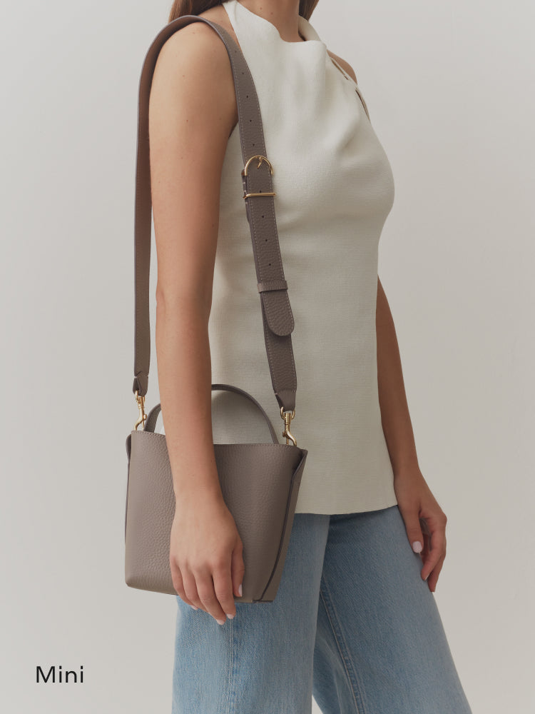 Model holding a small handbag with a long strap wearing a sleeveless top and jeans