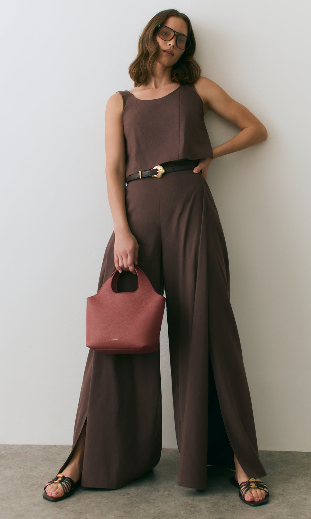 Person wearing a sleeveless top and wide pants, holding a handbag.