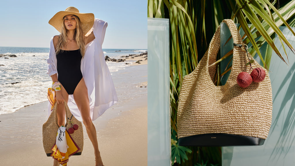 Woman in swimsuit and hat holds straw bag on beach; straw tote with pom-poms hangs nearby.