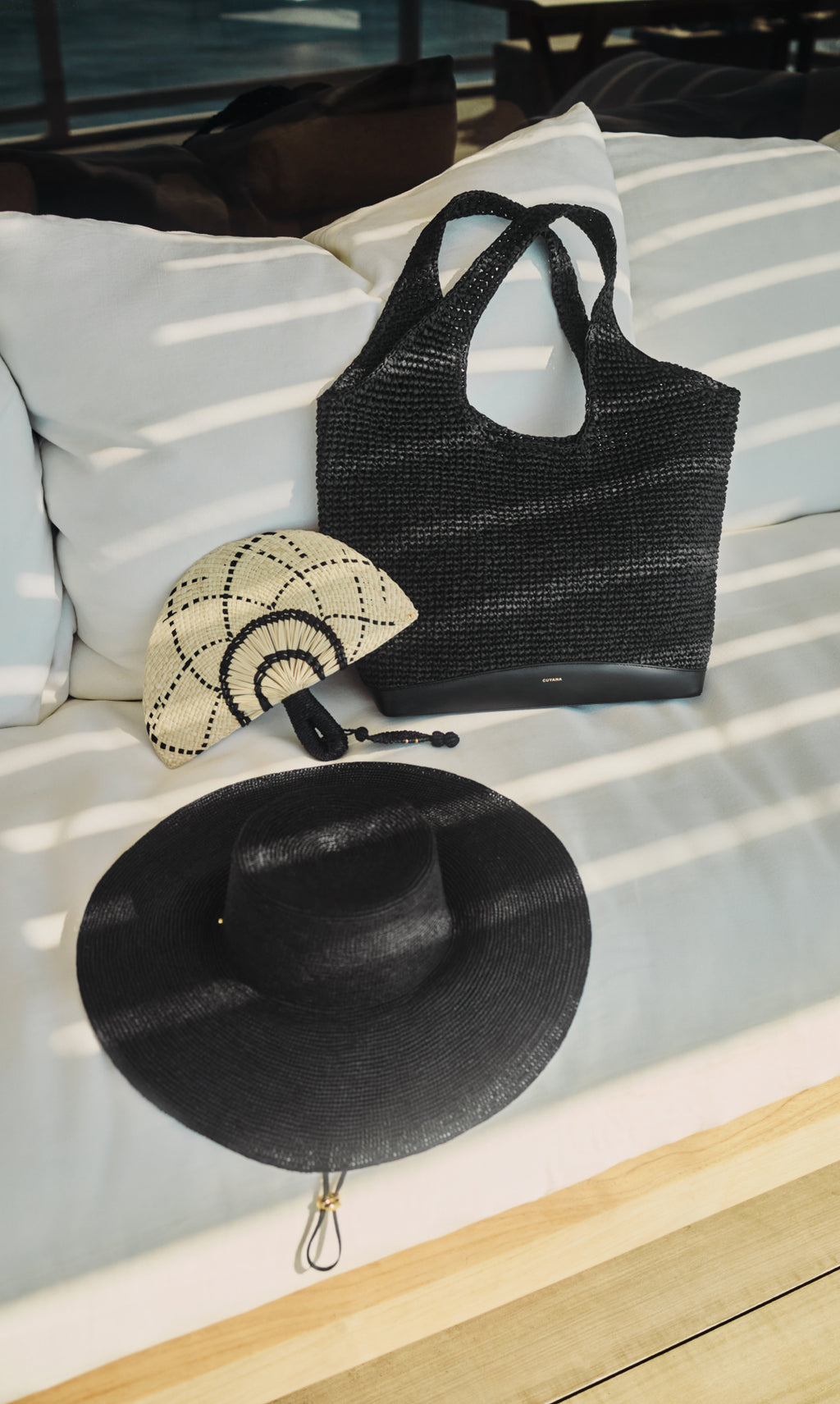 Woven tote, fan-shaped clutch, and wide-brimmed hat on a cushioned bench.