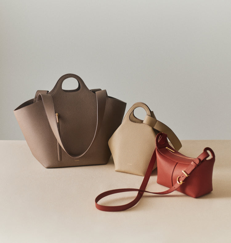 Three handbags in different shapes and sizes on a plain surface.