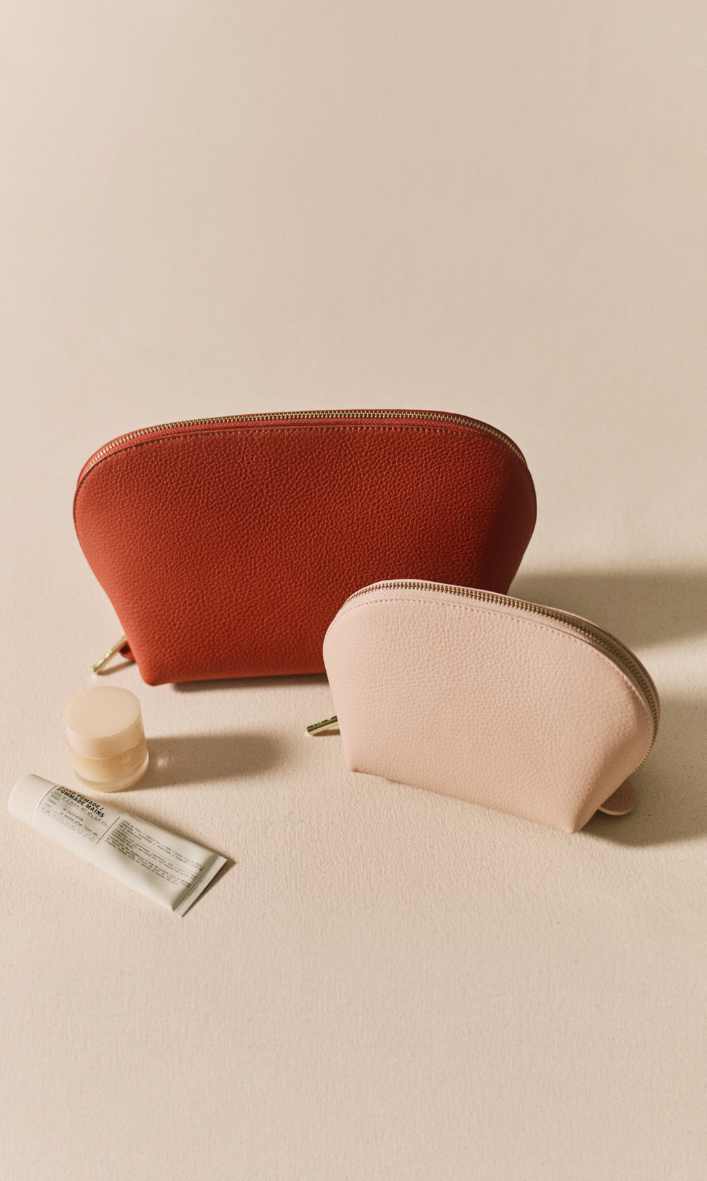 Two zipper pouches with a tube and container beside them.