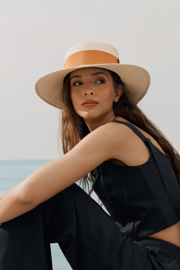 Woman wearing a brimmed hat looking over her shoulder by the sea.