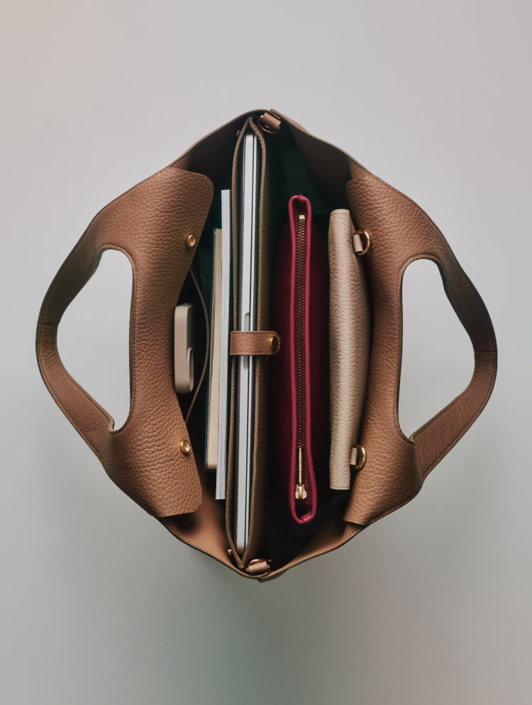 Open handbag viewed from above showing contents like laptop and pouches.