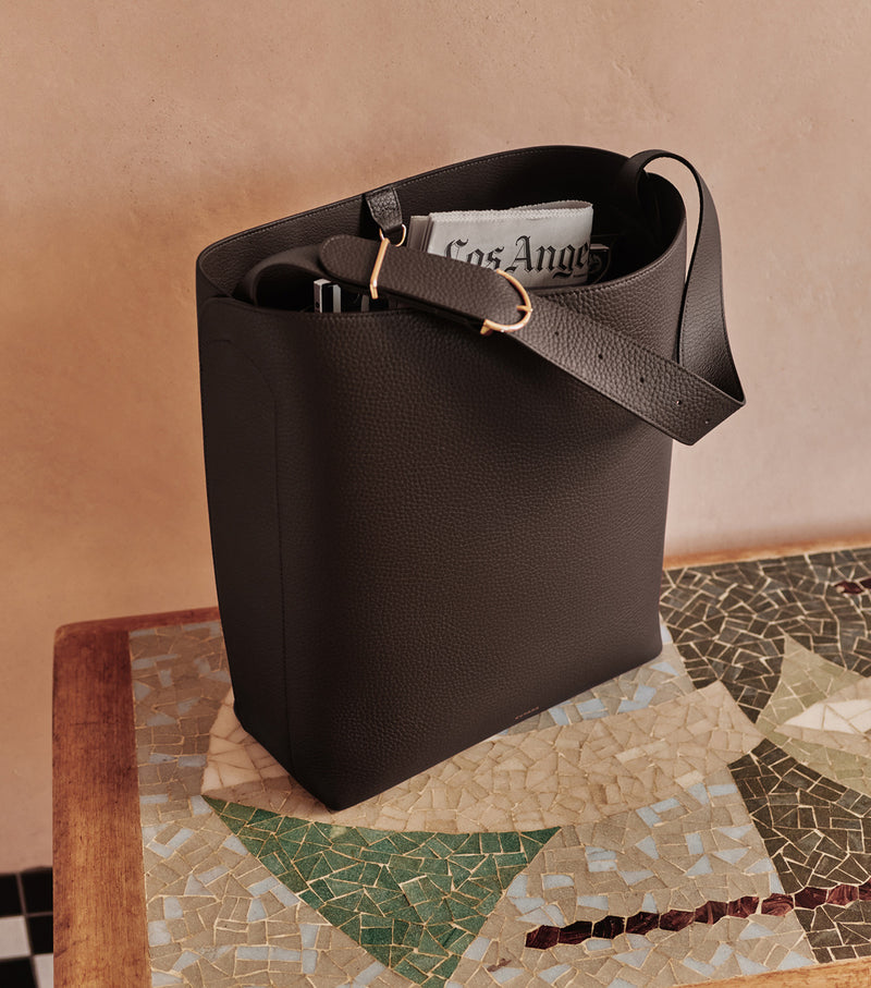 Tote bag on mosaic table with newspaper and items inside.