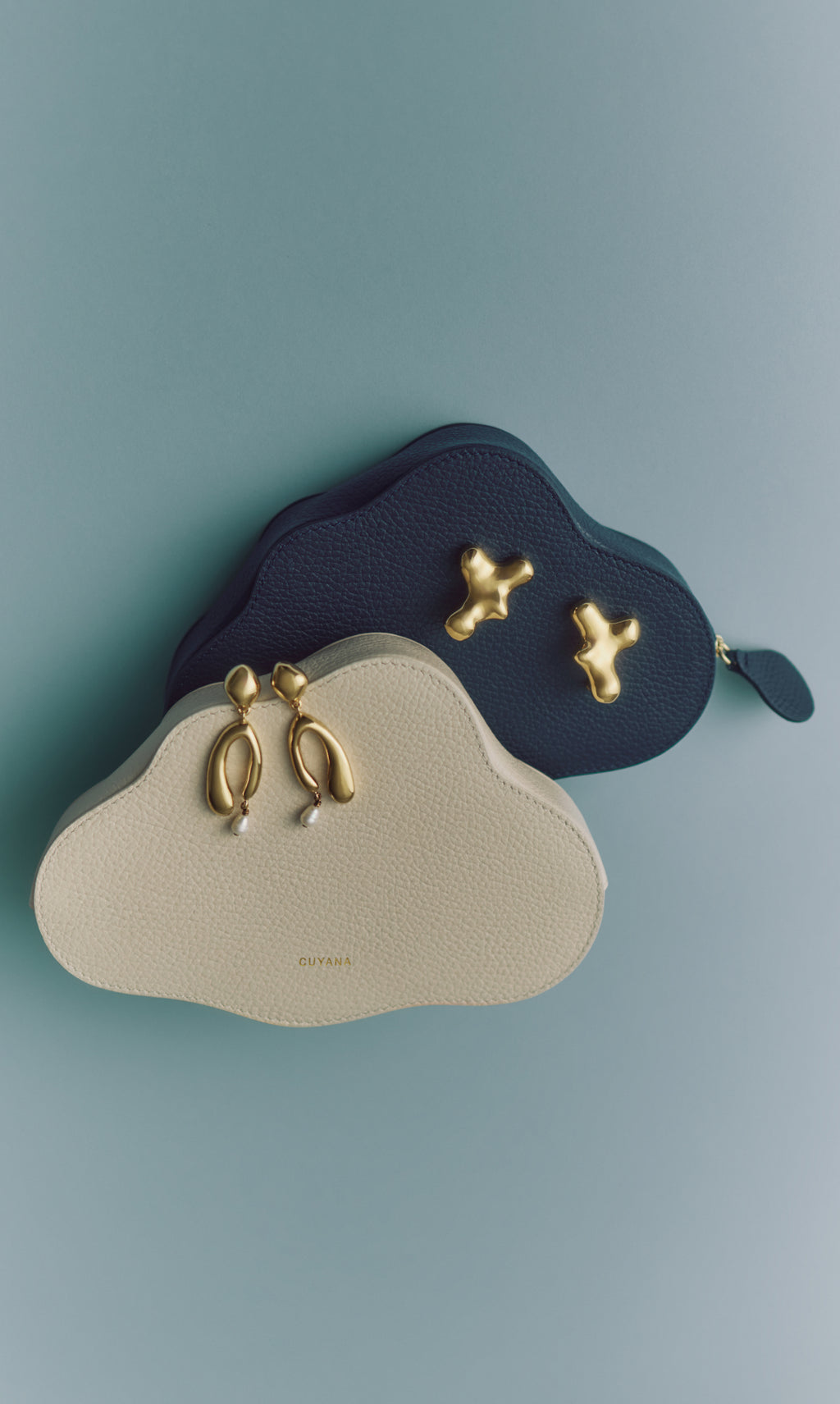Two cloud-shaped bags with abstract gold clasps on a flat surface.
