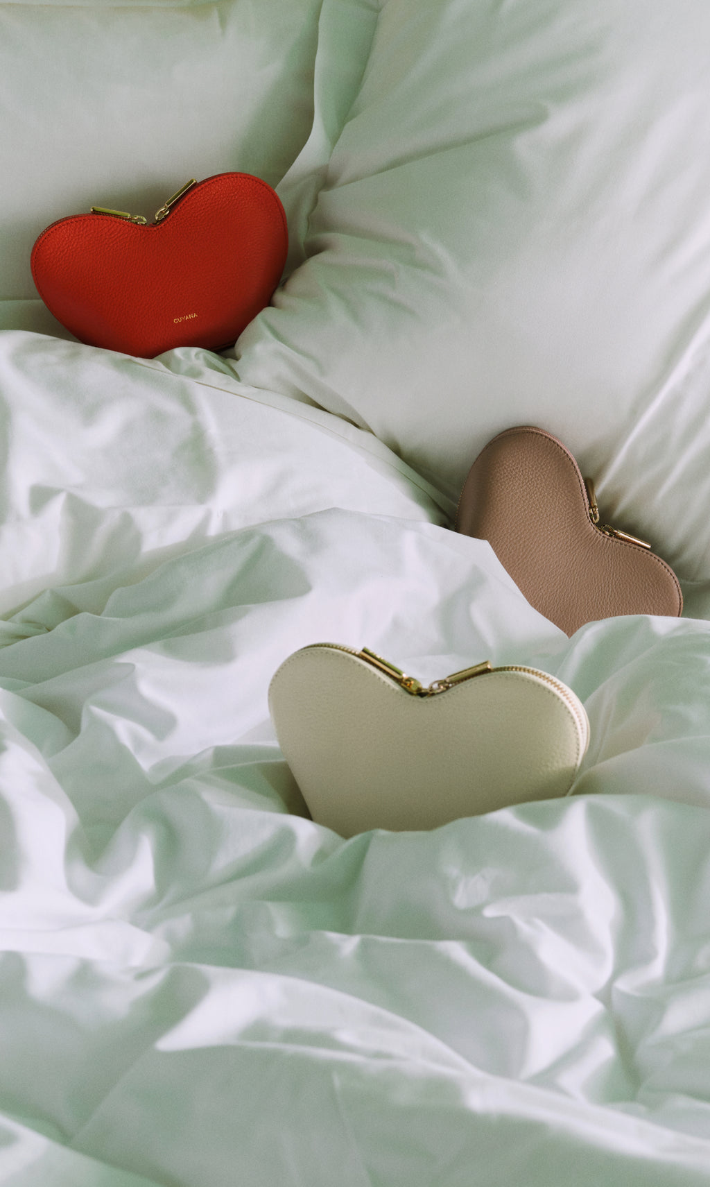 Three heart-shaped clutches on a bed.