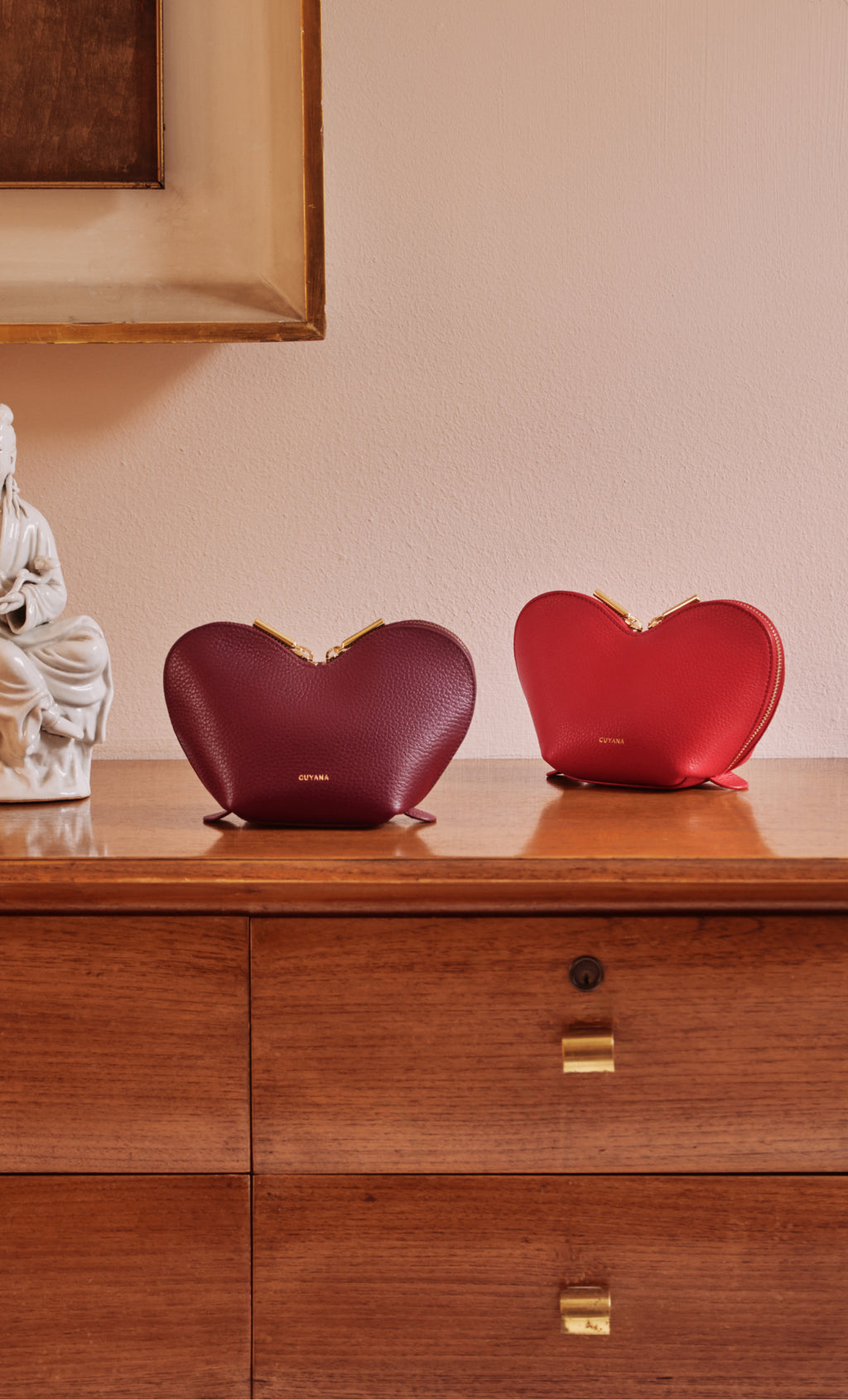 Two heart-shaped handbags on a wooden dresser next to a sculpture.