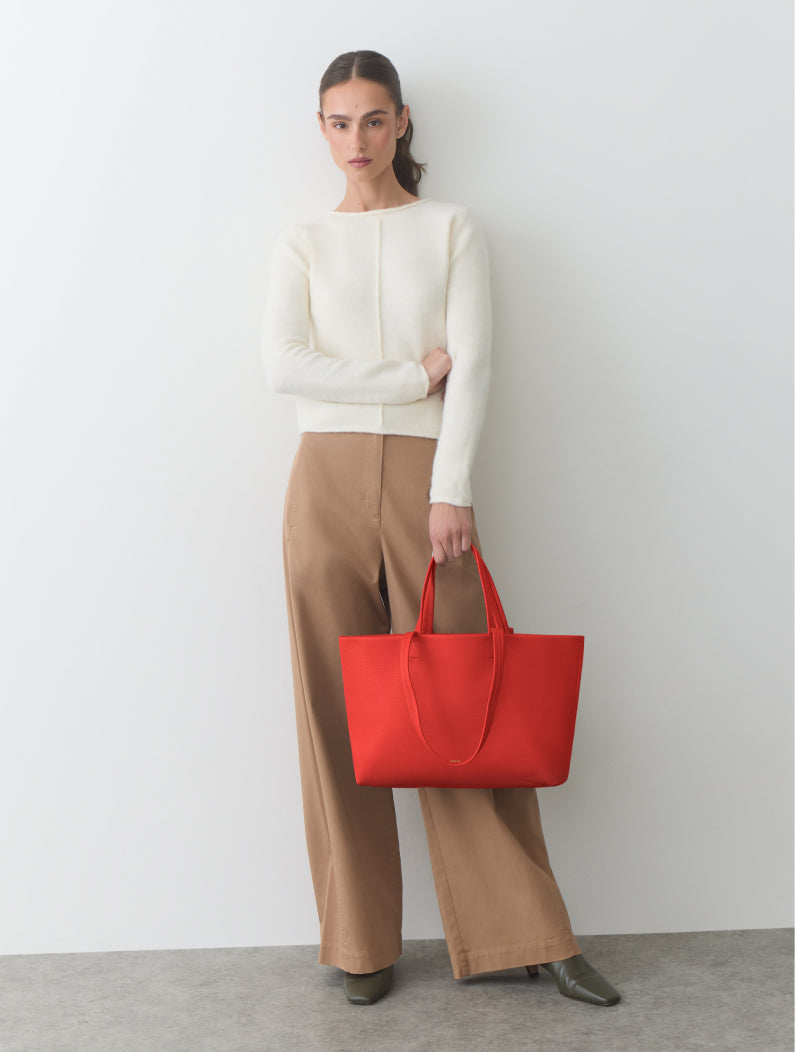 Person holding large tote bag, wearing a long sleeve top and wide-leg pants.
